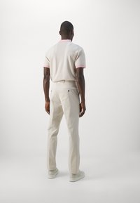 Pikétröja i ljusbeige med rosa accenter, matchad med ljusbeige byxor. Slät textur, figursydd design och minimal detaljer.