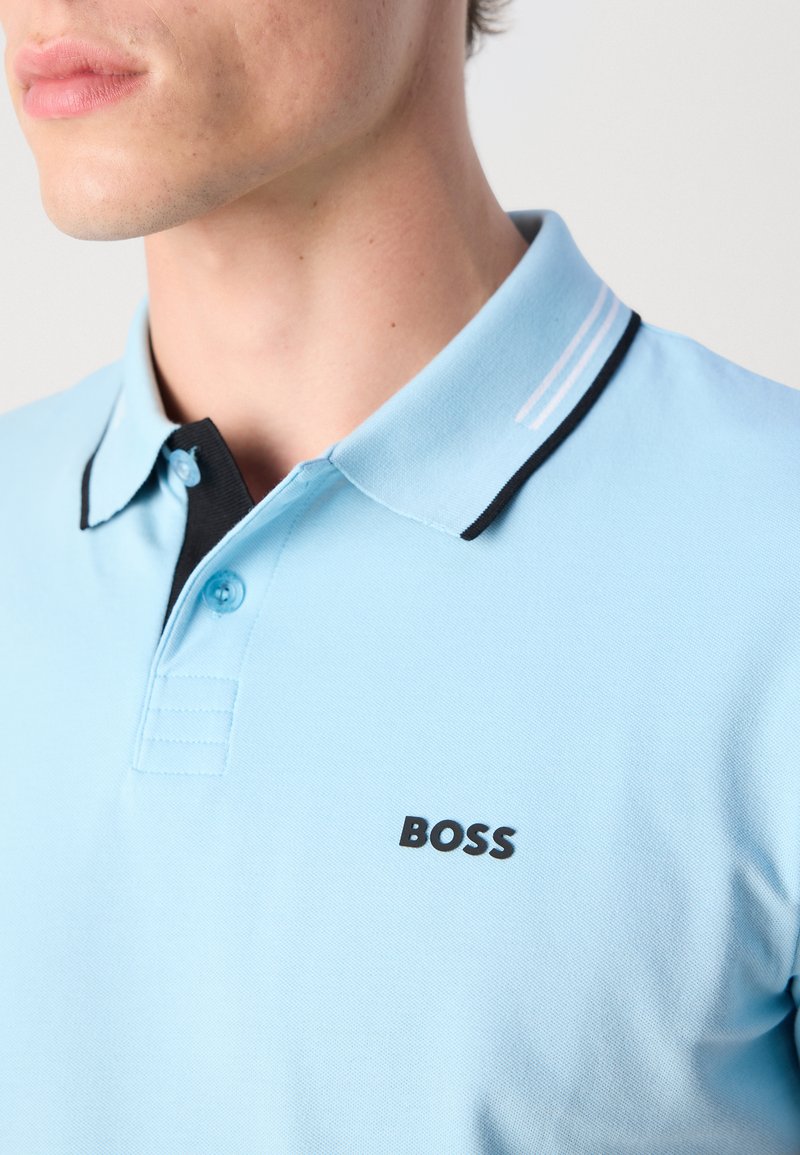 Polo shirt bleu clair avec un col noir, des rayures accentuées et un petit logo "BOSS" noir sur la poitrine. Fabriqué en tissu texturé.