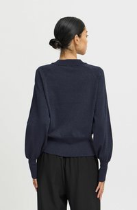 Marineblauer Pullover mit strukturiertem Finish, ausgestattet mit Ballonärmeln sowie gerippten Bündchen und Saum. Getragen mit schwarzen Hosen.