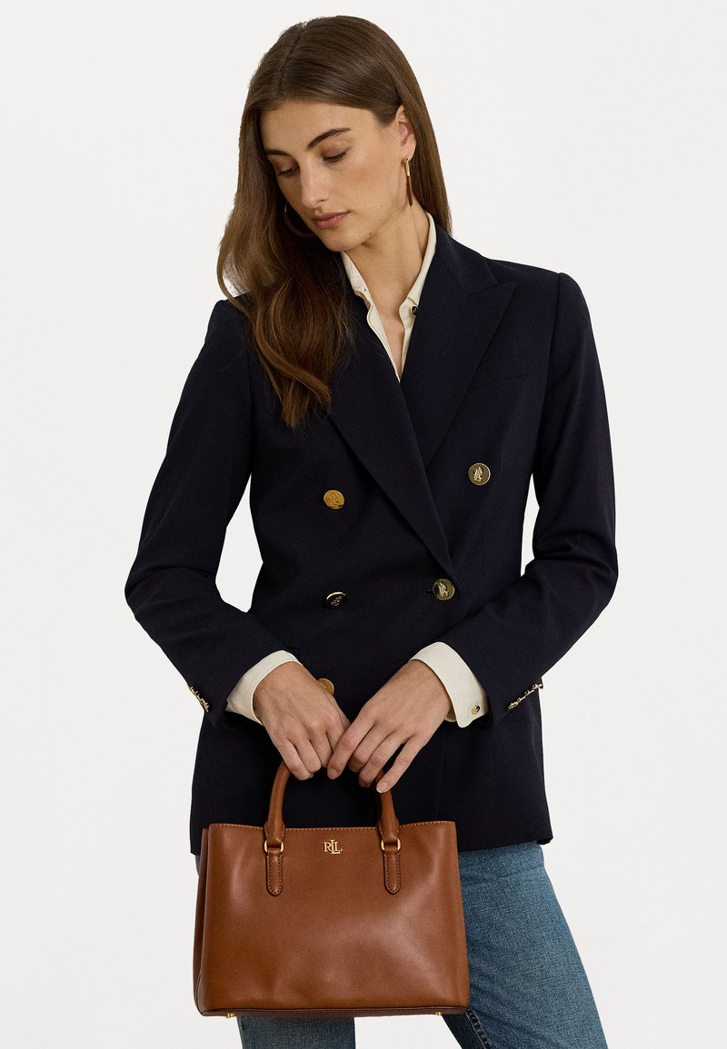 Jūras kara flotes divrindas žakete ar zeltītām pogām, ko apvieno ar brūnu ādas rokassomu ar zeltītu logotipu un strukturētu dizainu.