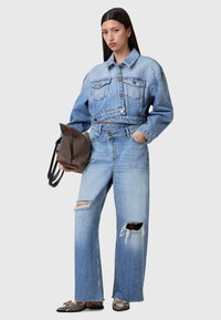 Chaqueta de mezclilla y jeans de pierna ancha en un lavado azul claro con detalles desgastados. Tejido texturizado con grandes bolsillos, acompañado de un bolso marrón.