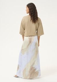 Beige oversized top met brede mouwen, gecombineerd met een lange, luchtige rok met een lichtblauw en beige abstract aquarelpatroon.