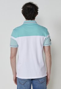 Turquoise színű felső résszel és fehér alsó résszel rendelkező pólóing, rövid ujjakkal és gallérral. Pamut keverék anyag.