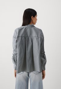Striped shirt with long sleeves, black and white vertical stripes, buttoned collar, and relaxed fit. Paired with light blue denim pants.