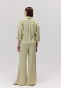 Jasnozielona, luźno dopasowana koszula z krótkim rękawem oraz spodnie z szerokimi nogawkami o gładkiej teksturze i swobodnym kroju. Widok z tyłu z minimalnymi detalami.