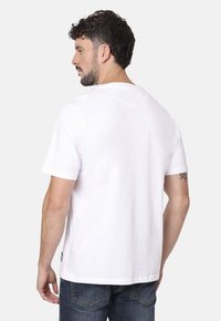 Camiseta de algodón blanca con mangas cortas, cuello redondo y un corte holgado. Presenta una abertura lateral y una pequeña etiqueta de marca en el dobladillo.