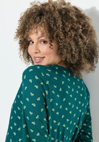 Lange mouwen teal shirt met een subtiel bloemenpatroon. Gemaakt van zacht, textuurstof met een relaxte pasvorm en ronde halslijn.