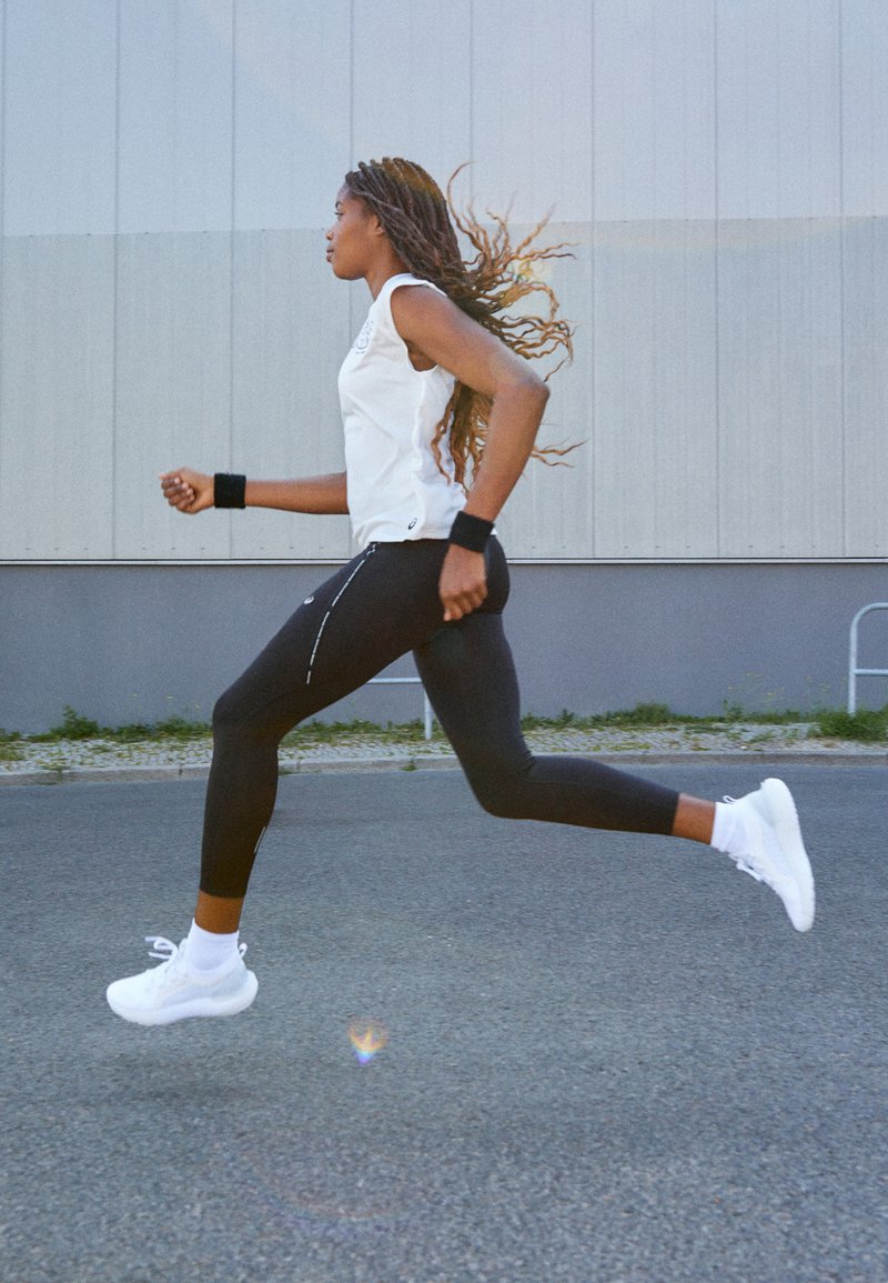 Completo sportivo con top senza maniche bianco, leggings neri e sneakers bianche. Dettagliato con polsini e accenti riflettenti sui leggings.