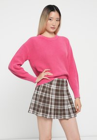 Suéter rosa canelado de mangas longas combinado com uma saia plissada quadrada castanha com detalhes em branco e preto. Textura suave e design casual.