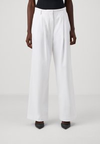 Pantalones de pierna ancha blancos con pliegues, una textura suave y una cinturilla ajustada. Combinados con tacones negros puntiagudos para un contraste.