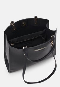 Svart lær tote bag med teksturert finish, gullhardware og en enkelt stropp. Innvendig inkluderer glidelås- og åpne lommer.