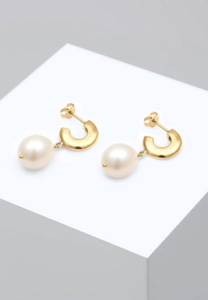 Boucles d'oreilles en or en forme de courbe, reliées à une grande perle blanche brillante, avec une texture lisse et une finition polie.