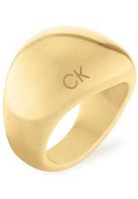 Złoto-tonowany pierścionek o gładkim, zaokrąglonym kształcie z logo CK. Powierzchnia jest wypolerowana, odbijając światło z elegancką fakturą.