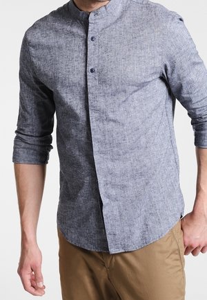 Camisa de hombre de manga larga en tejido azul texturizado, con cuello alzado y cierre de botones en la parte delantera. Presenta mangas enrolladas y un corte ajustado.