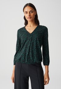 Blusa nera con scollo a V, caratterizzata da un motivo astratto verde. Maniche a tre quarti e dettaglio in vita arricciato, realizzata in tessuto leggero.