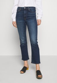 Jeans de tiro alto en azul oscuro con corte recto, que presentan un ligero desvanecimiento, cinco bolsillos y un sutil detalle de botón en la cintura.