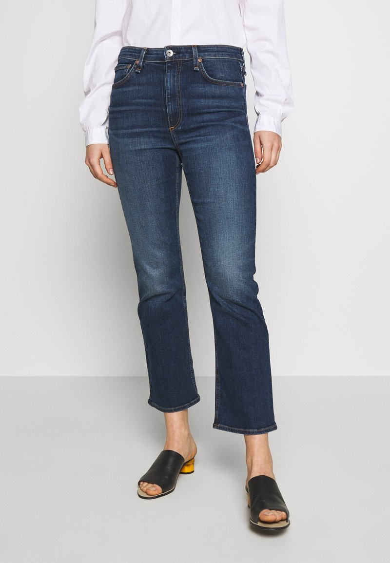 Jeans de tiro alto en azul oscuro con corte recto, que presentan un ligero desvanecimiento, cinco bolsillos y un sutil detalle de botón en la cintura.
