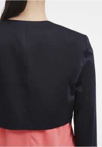 Marinblå cropped jacka med en slät yta, tillsammans med ett rosa plagg. Klara linjer och minimal detaljering på ryggen.