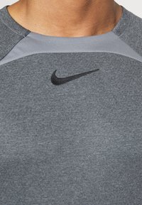 Grå sporttröja med rund halsringning. Har en ljusgrå axelkant och en svart Nike-logga på bröstet. Mjuk textur.