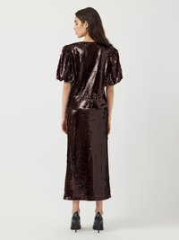 Abito marrone con paillettes, con maniche corte a palloncino, lungo fino al ginocchio. Texture liscia e silhouette aderente. Indossato con scarpe col tacco alto nere.