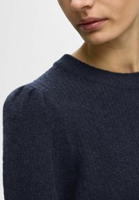 Maglione lavorato a maglia blu navy con colletto a coste e dettagli di maniche leggermente a sbuffo. Morbido al tatto e con un aspetto accogliente.