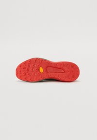 Semelle de sneaker grise avec une surface texturée rouge et le logo Vibram ; comporte des crampons ronds pour une adhérence et une section de talon intégrée lisse.
