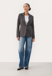 Šedý přizpůsobený blazer s jedním stříbrným knoflíkem, nošený přes bílé tričko; doplněný širokými modrými džíny a černými balerínkami.