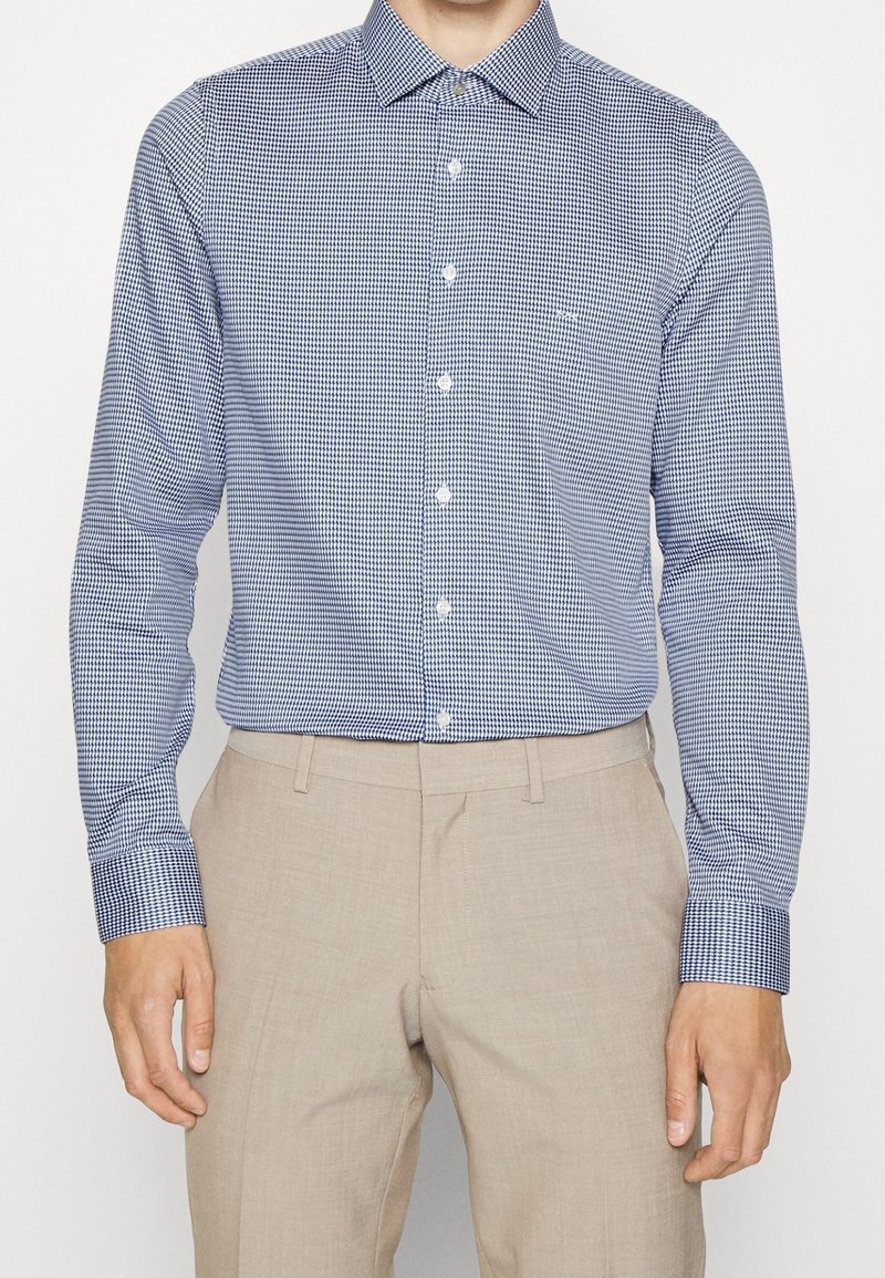 Blå och vit rutigt långärmad skjorta med spetsig krage, knappstängning framtill och kontrasterande manschettdetalj, tillverkad av ett slätt tyg.