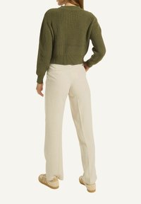 Olivgrüner, gerippter Pullover mit langen Ärmeln, kombiniert mit hellbeigen, weit geschnittenen Hosen. Die Schuhe sind braun mit einem strukturierten Design.