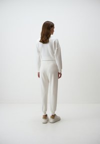 Witte sweatshirt met verlaagde schouders, gecombineerd met smalle witte broek. Bevat elastische manchetten en tailleband, gedragen met witte sneakers.