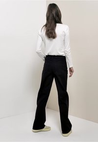 Pantalones negros de pierna ancha con cintura alta y bolsillos traseros. Combinados con una camisa blanca ajustada de manga larga y zapatillas de color claro.
