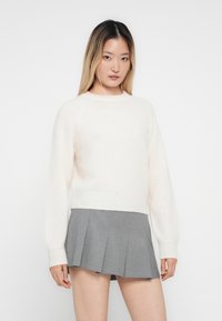 Crème-kleurig, zacht sweater met een ronde hals en raglanmouwen, gecombineerd met een geplooide grijze rok. Glad textuur, ontspannen pasvorm.