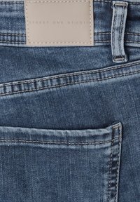 Džínovina středně modré barvy s viditelnými stehmi. Nad zadní kapsou je kožená značka s raženým nápisem "STREET ONE STUDIO".