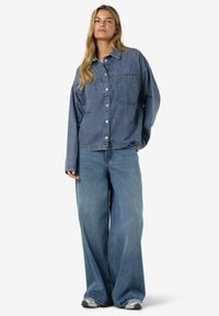 Jeansskjorta i ljusblått med krage, två framfickor och vida jeans med lös passform, kombinerat med grå sneakers.