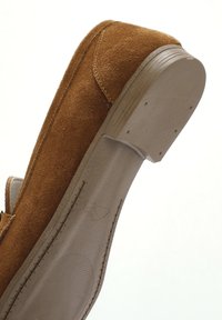 Bruine suede instap-schoen met een gladde, beige rubberen zool. Kenmerken zijn onder andere contrasterende stiksels en een iets verhoogde hak.