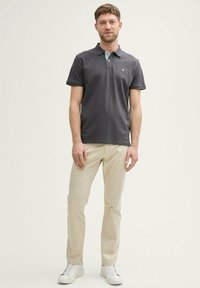 Mørk grå polo skjorte med en turkise krave, parret med lyse beige bukser og hvide sneakers, med et logo på skjorten.