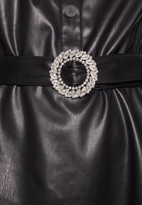 Ceinture en cuir noir avec une boucle ronde ornée de strass clairs en forme de marquise et ronds, présentant une finition texturée.