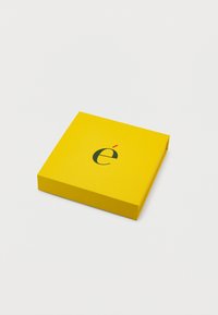 Κίτρινο τετράγωνο κουτί με ένα μαύρο πεζό γράμμα "é" και μια μικρή κόκκινη τονική στο καπάκι του, σε απλό λευκό φόντο.