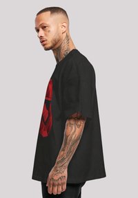 Černé oversized tričko s velkým červeným geometrickým grafickým motivem na přední straně. Krátké rukávy a volný střih, vyrobeno z bavlněné tkaniny.