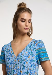 Abito floreale blu con scollatura a V, maniche corte a sbuffo con dettagli a fantasia e bottoni lungo la parte anteriore. Tessuto dalla superficie liscia.
