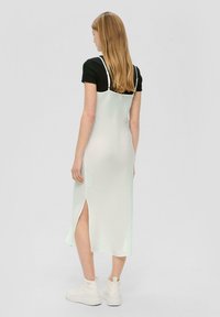 Robe en satin vert clair avec des bretelles fines, fente sur le côté, portée sur un haut noir à manches courtes, associée à des baskets blanches épaisses.