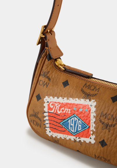 Ruskea nahkalaukku, jossa on kullattu vetoketju, esittelee värikästä leimauskuviota, jossa lukee "MCM" ja "1976". Laukussa on myös kohokuvioituja logoja ja timanttikuvioita.