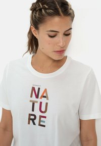 Hvid bomulds t-shirt med et multifarvet teksttryk "Empowered by NATURE" med forskellige former, i blødt stof og klassisk crew neck design.