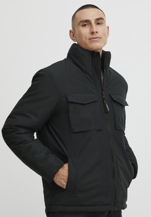 Black insulated jacket with a high collar, front zip closure, and two chest pockets. The material appears smooth with a matte finish.