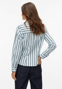 Jasnoniebieska koszula z pionowymi granatowymi paskami, długimi rękawami, zapinanymi na guziki mankietami oraz detalem yoke na plecach, zestawiona z ciemnymi dżinsami.