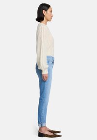 Maglione a treccia crema, jeans azzurri chiari e ballerine a punta con stampa leopardata. Vista laterale che evidenzia le maniche lunghe e i jeans risvoltati.