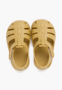 Sandalias de goma amarillas con punta cerrada y tira trasera, que cuentan con cortes horizontales y verticales para la transpirabilidad y detalles en la textura.
