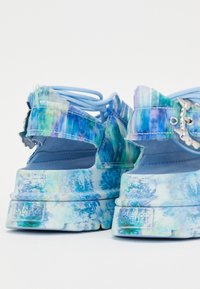 Sandales compensées bleues à finition brillante, dotées d'un motif floral texturé, de brides ajustables et d'accents de ferrures distincts.
