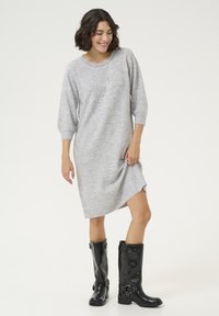 Robe pull grise à manches trois-quarts, dotée d'une texture douce et d'une fente latérale, associée à des bottes de pluie noires en cuir verni jusqu'aux genoux.
