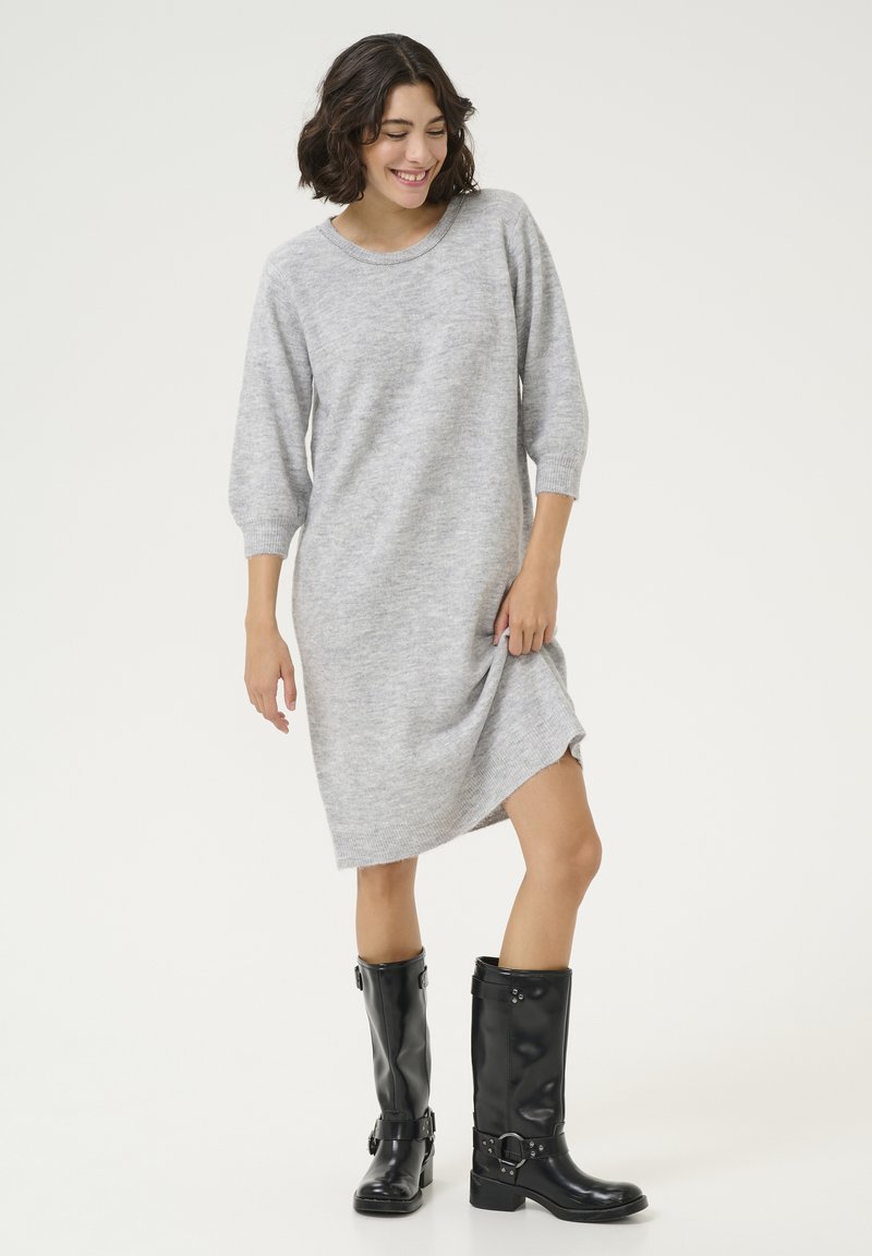 Robe pull grise à manches trois-quarts, dotée d'une texture douce et d'une fente latérale, associée à des bottes de pluie noires en cuir verni jusqu'aux genoux.
